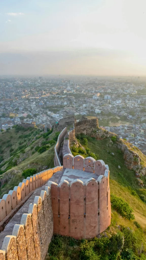 Panoramic view of a historic fortress wall and battlements on a hill overlooking a dense city at sunrise or sunset.