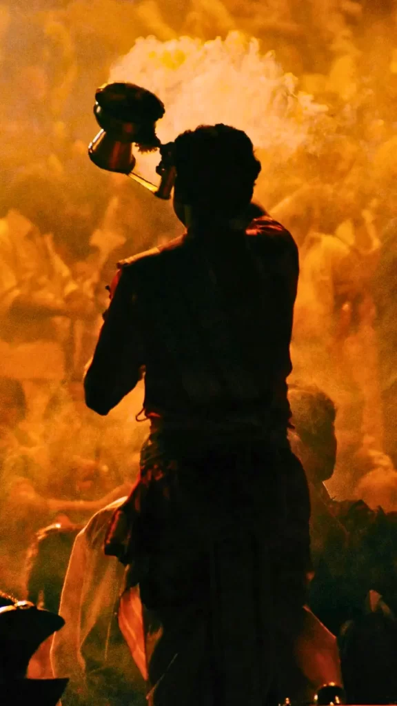 Silhouette of a person performing a traditional ritual or Aarti ceremony with a pot, surrounded by golden smoke and people.