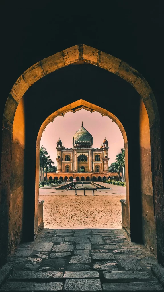 View through a dark archway of a beautiful historic Mughal-style tomb or monument at sunset.